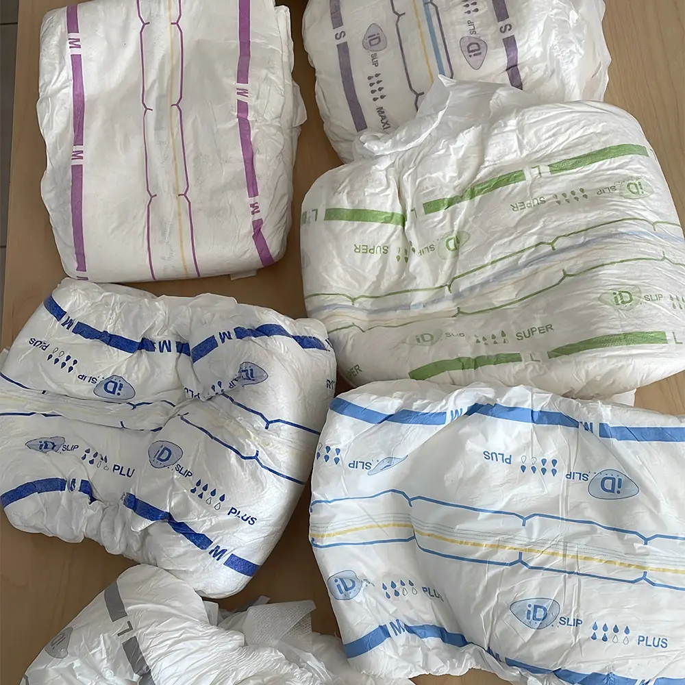 Various adult diapers with colored size markings and absorbency indicators laid out on a wooden surface.
