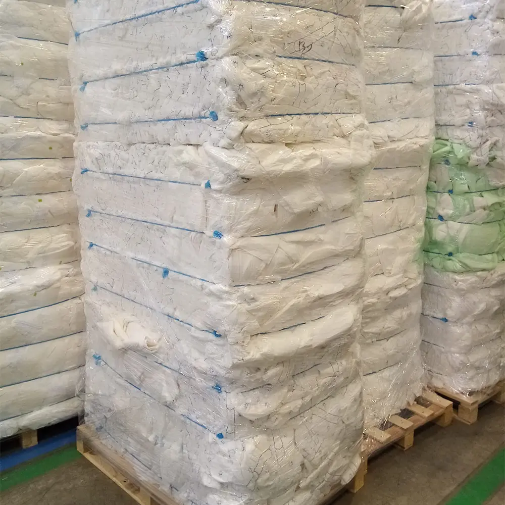Stacks of large white and some green plastic-wrapped bundles on wooden pallets in a warehouse.