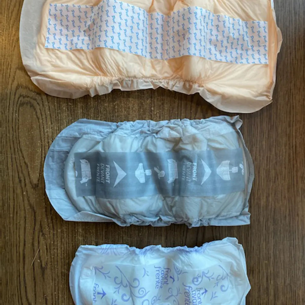Three adult diapers of different designs and colors laid out on a wooden surface.