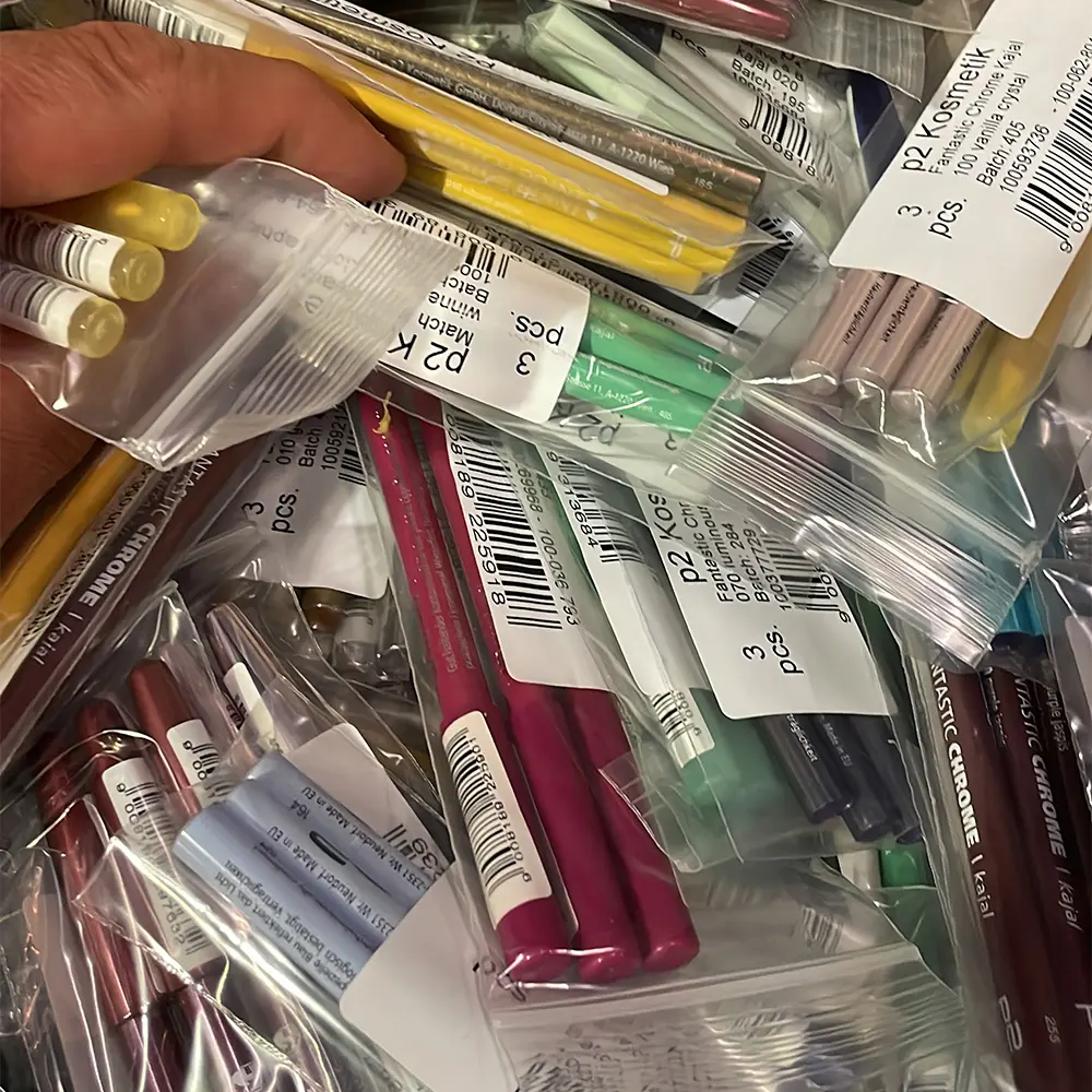 Hand holding plastic bag with yellow cosmetic pencils among various packaged cosmetic pencils in multiple colors.