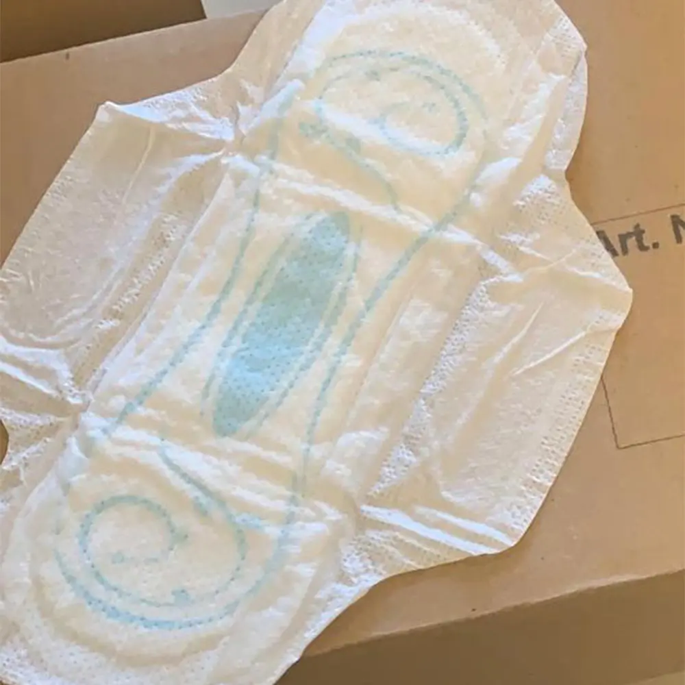 White sanitary pad with light blue absorbent patterns placed on a cardboard box.