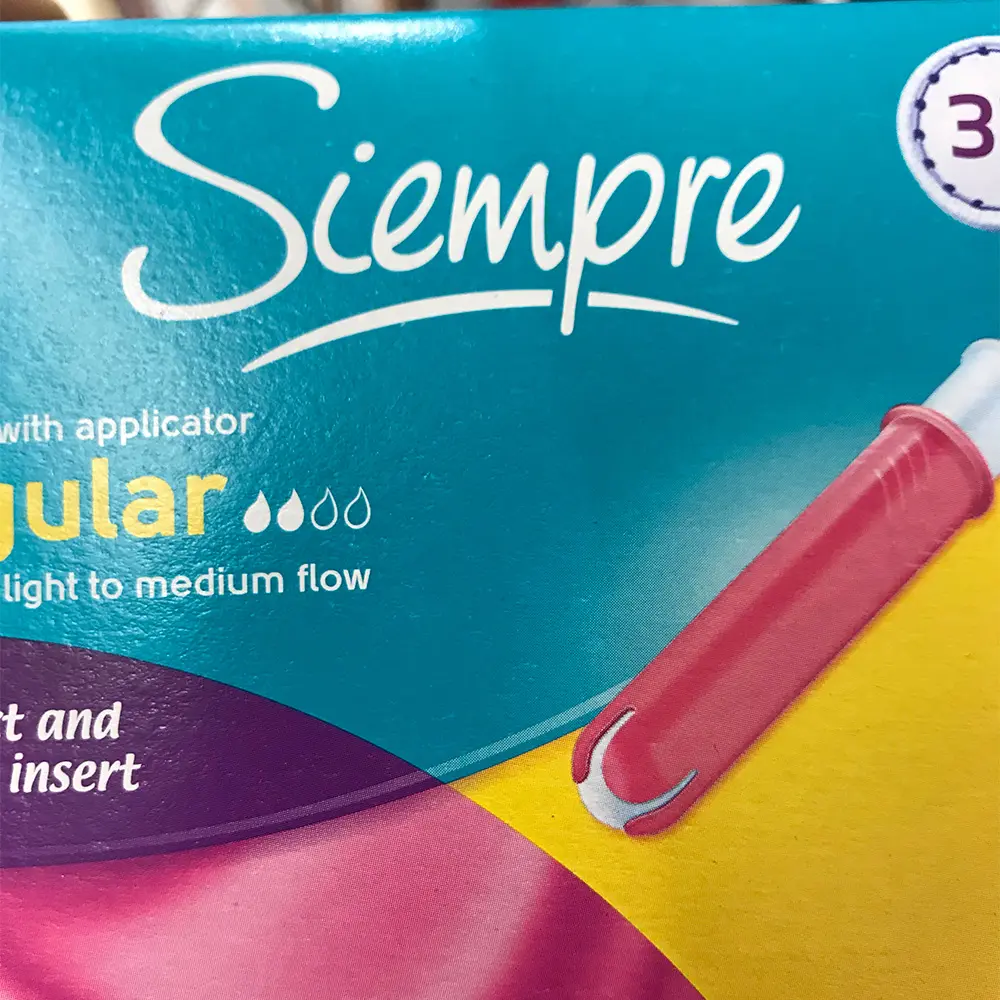Close-up of Siempre menstrual product packaging showing a red applicator and text indicating regular flow for light to medium use.
