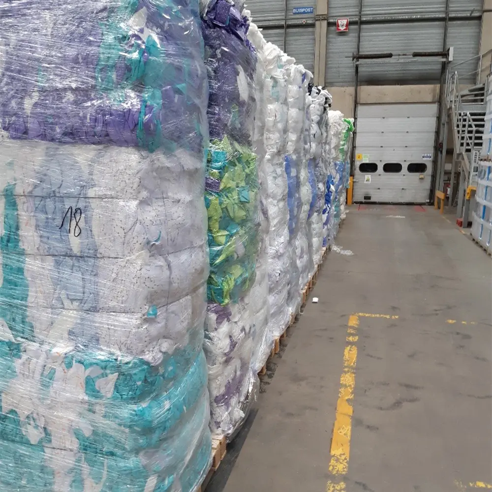 Large pallets of compressed plastic wrapped in clear plastic stacked in a warehouse near a closed industrial door.