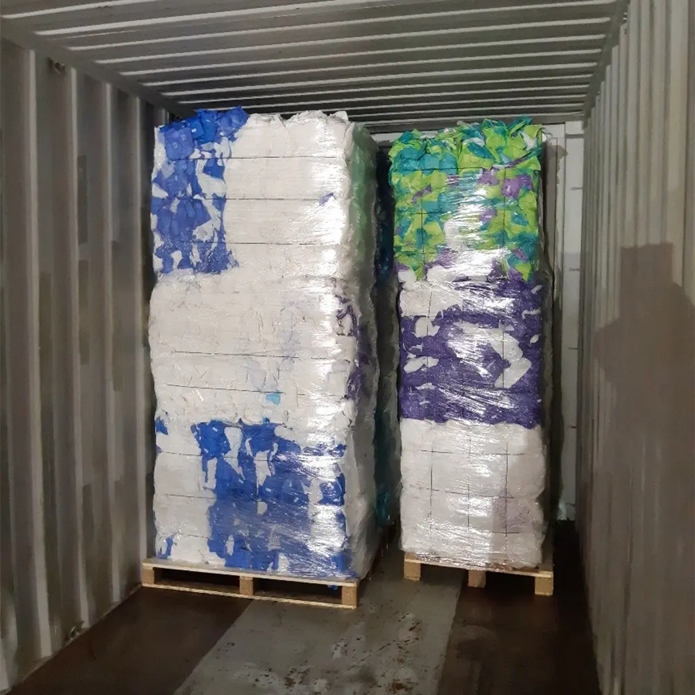Two large pallets wrapped in plastic containing white and colored materials stacked inside a shipping container.