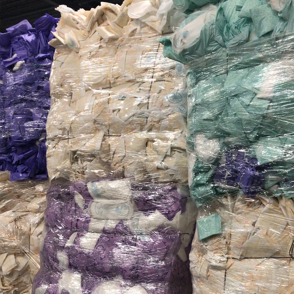 Bales of various colored folded disposable diapers wrapped in clear plastic in a warehouse.