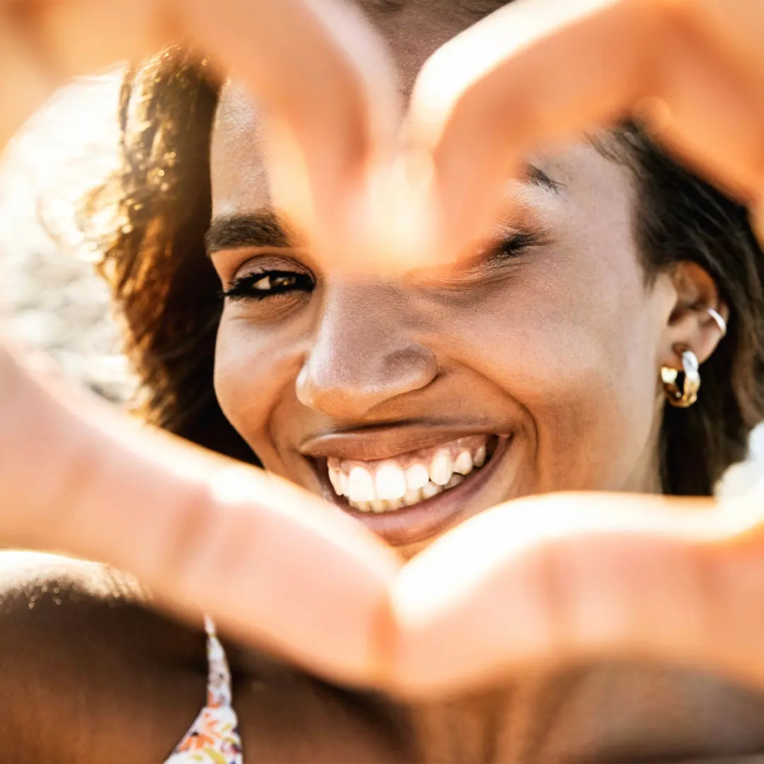 Smiling woman making a heart shape with her hands, framing her face.