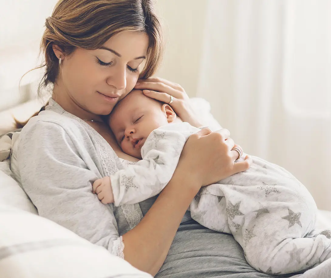 Mother gently cradling and holding her sleeping baby wrapped in star-patterned pajamas.