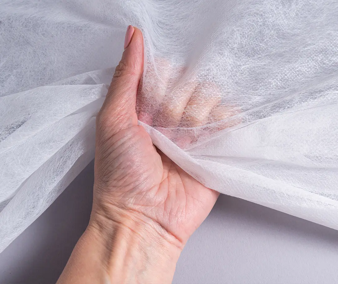 Smiling woman with curly hair applying white cream to her cheek against a beige background.