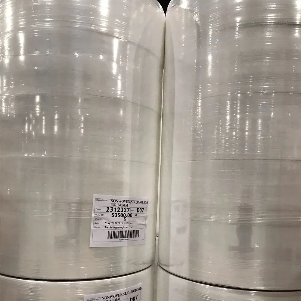 Large rolls of clear or white nonwoven fabric stacked vertically with labels indicating product details.
