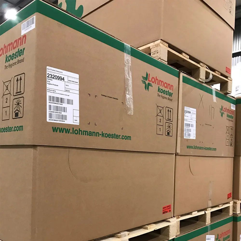 Stacked brown cardboard boxes labeled Lohmann Koester, The Hygiene Brand, on wooden pallets in a warehouse.