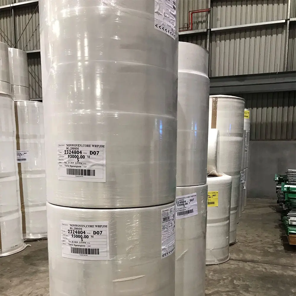 Large rolls of white nonwoven fabric stacked in a warehouse.