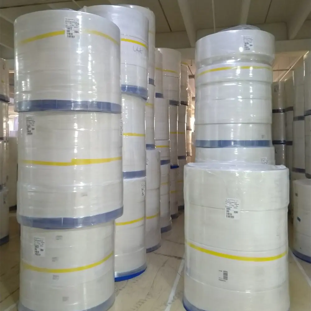 Stacks of large white rolls of industrial material with yellow and blue bands stored in a warehouse.