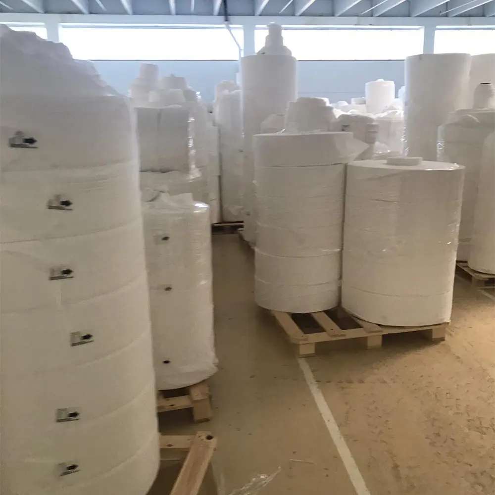 Large industrial rolls of white nonwoven fabric stacked on wooden pallets inside a warehouse.