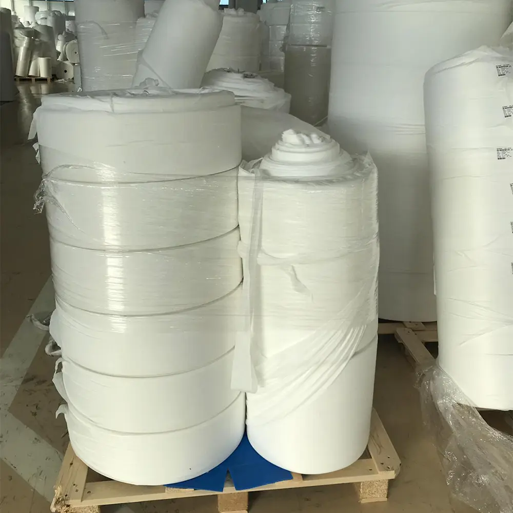 Large rolls of white nonwoven fabric stacked on a wooden pallet in a warehouse.